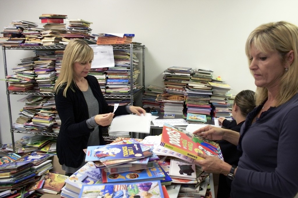 Newport Beach residents Lisa Zielinski (right), Cassie Conant (left) and Emily Conant, 16, of Newport Harbor High School, go through and put ALNM stickers on books before packing them up to be delivered.