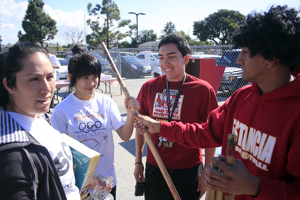 Arts and music program director of SOY, Eduardo “Eddie”  Iniestra hands a walking stick to Brenda Vargas, 17, as Frank Alvarez, 18, looks on and they chat about an upcoming SOY event, while Operations Manager of SOY, Silvia Rosales, directs work elsewhere.