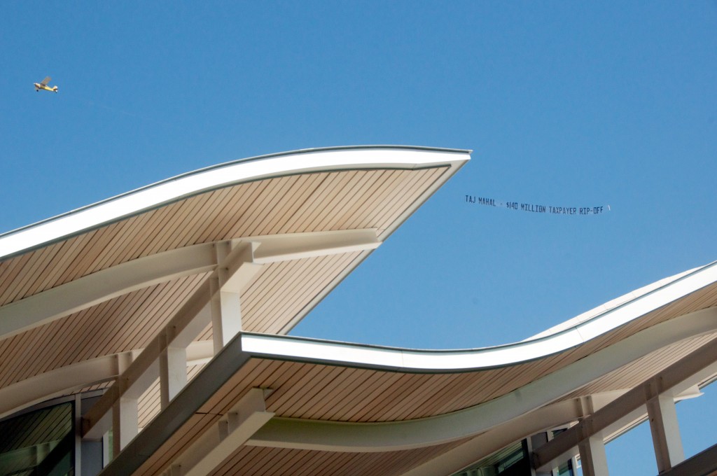 A plane flies above the new civic center on Saturday during the ceremony towing a banner reading, "Taj Mahal - $140 million taxpayer rip-off" — Photo by Amy Senk