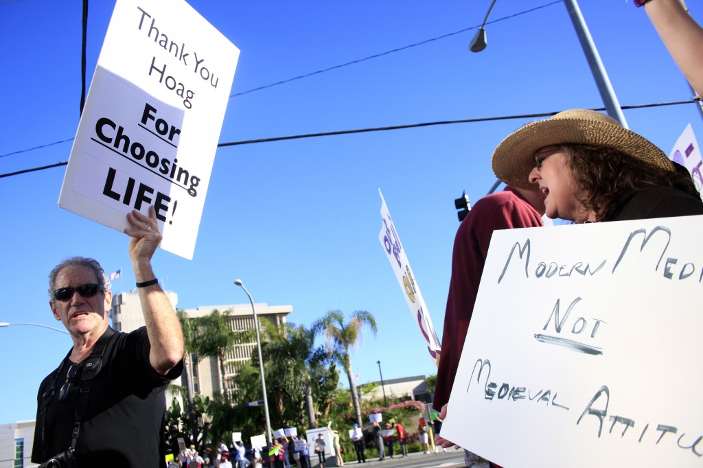 A Hoag Memorial Hospital Presbyterian supporter (left) and a protestor wave signs at each other outside the hospital in June. Demonstrators later picketed outside a local doctor's home, yelling, writing slurs on the sidewalk in chalk, and causing a disturbance.<br />Photo by Sara Hall