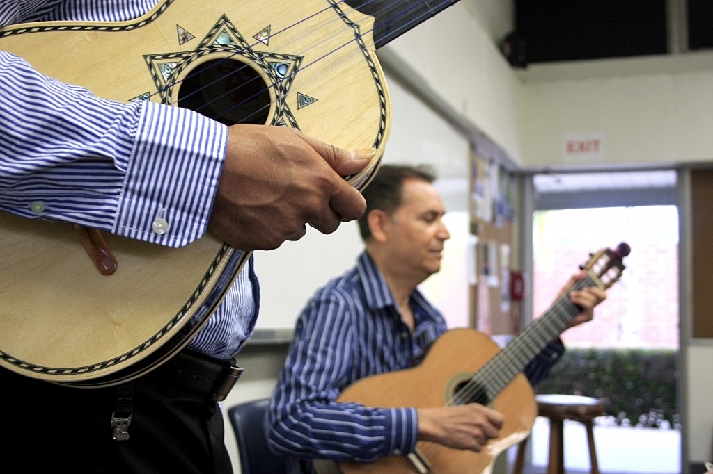 Guitar instructor Jesse Hernandez plays a portion of a song to the Advanced Armonia class as Anthony Zuniga holds his vihuela as he waits to teach the students his part.