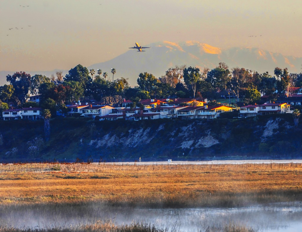 A plane takes off from John Wayne Airport in February, flying over Newport Beach homes and the Upper Newport Bay. — Photo by Lawrence Sherwin