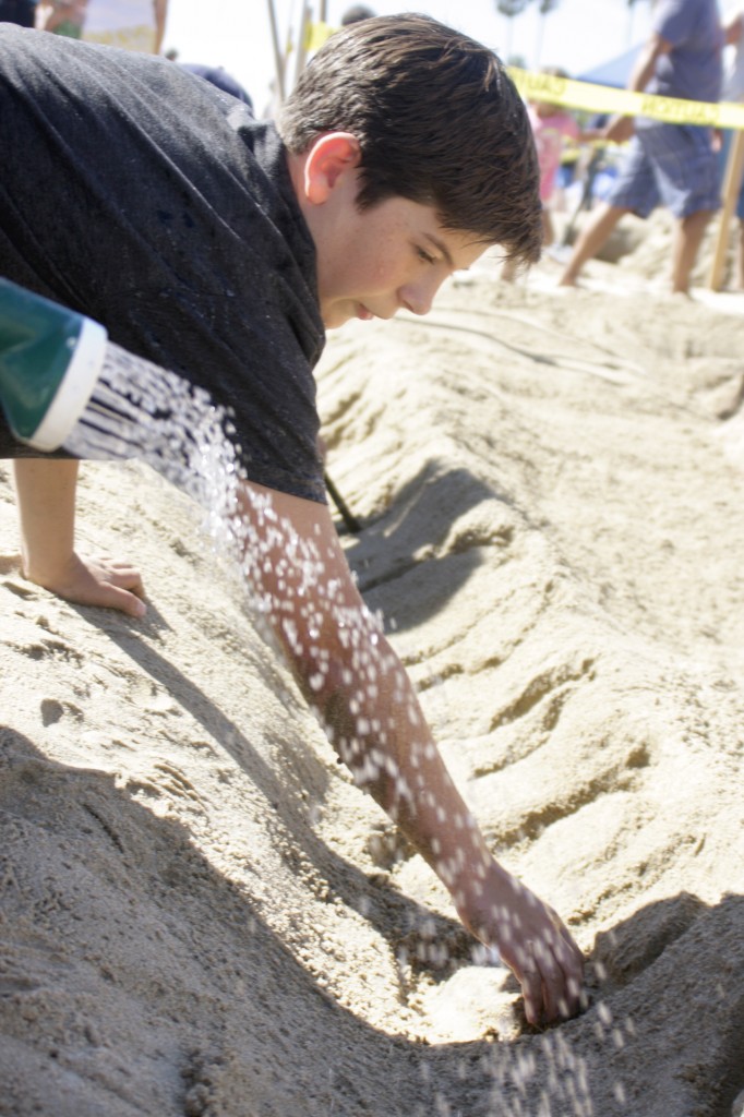 Team members work together as one writes and another waters down the dry sand.