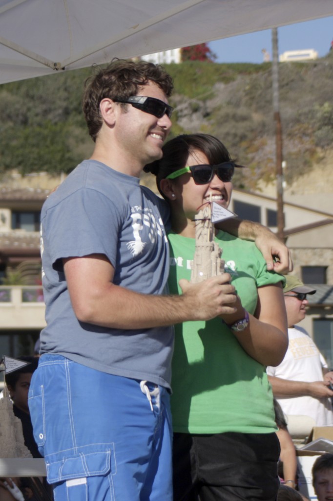 An excited couple poses for photos after winning a trophy.