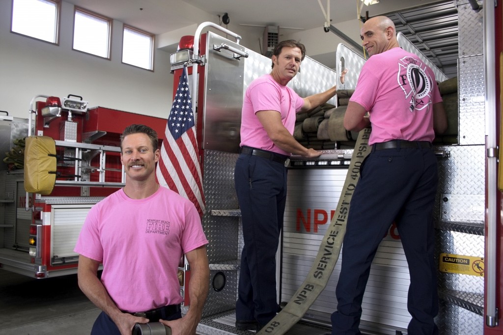 :(left to right) Newport Beach Fire Department paramedic J.C. Nessa, engineer Alan Baker and fire investigator Capt. Mike Liberto adjust equipment on the back of the fire engine and pose for a photo while wearing their pink Breast Cancer Awareness shirts.   — Photos by Sara Hall