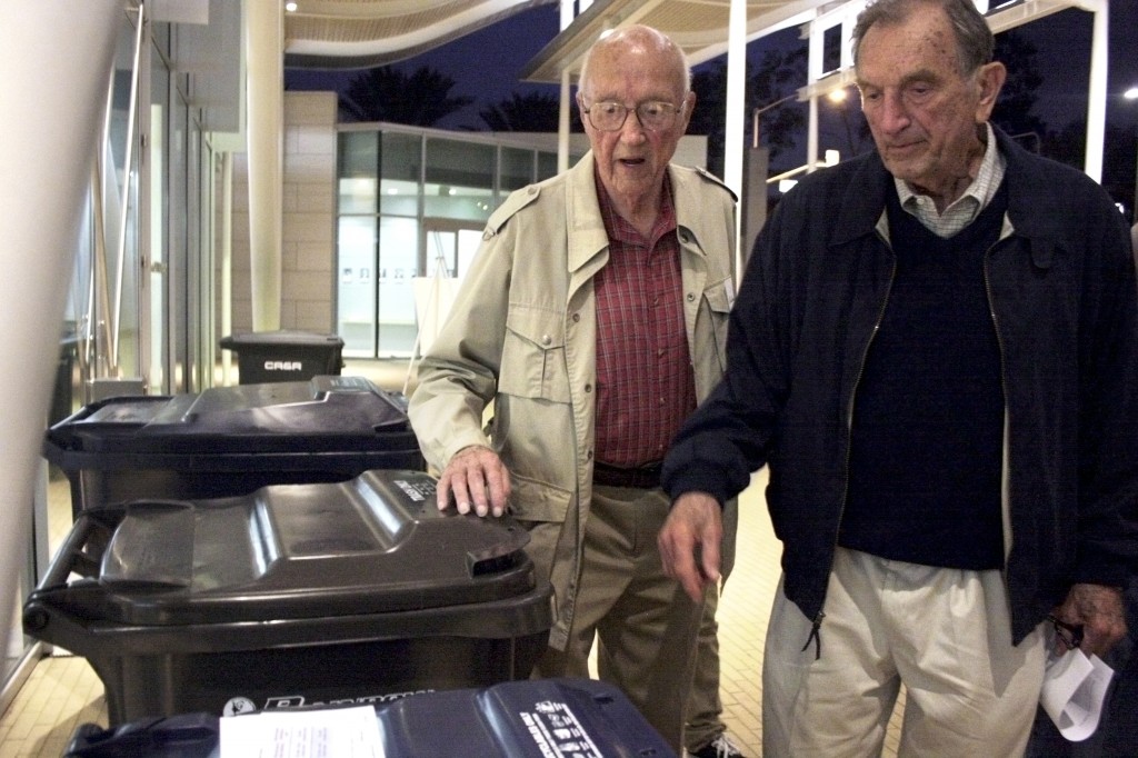 Residents Wally Olson (left) and Val Skoro inspect the trash bins on display outside the community room at the civic center after the Speak Up Newport meeting about outsourcing the city’s trash collection service concluded on Wednesday night. — Photos by Sara Hall