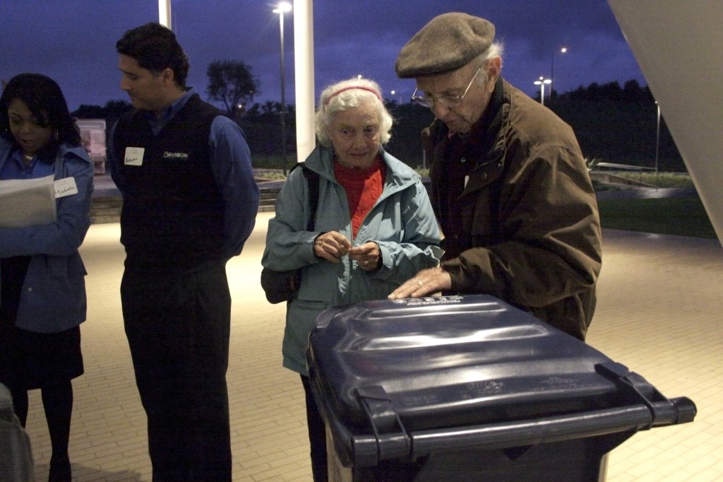 Ginny K. (middle) and a man who wished to remain unnamed examine trash bins as Rainbow Disposal staff (left) speak with residents after the Speak Up Newport meeting about outsourcing the city’s trash service