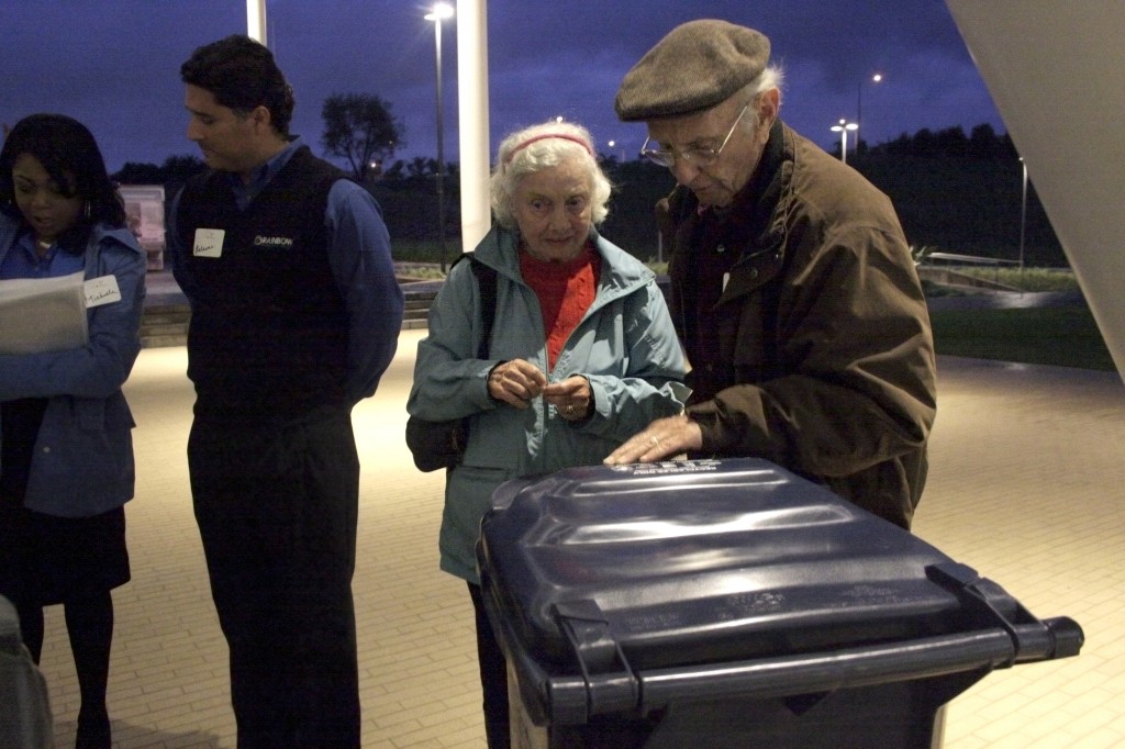 Ginny K. (middle) and a man who wished to remain unnamed examine trash bins as Rainbow Disposal staff (left) speak with residents after the Speak Up Newport meeting about outsourcing the city’s trash service  