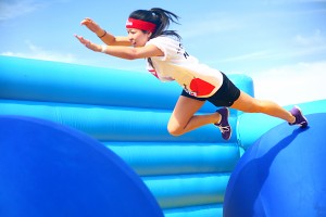 A woman leaps toward the second ball of the Bouncy Bridge obstacle.