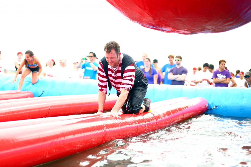 Ted Dixon crawls over a floating plank while avoid the oversized red rubber balls swinging above him.