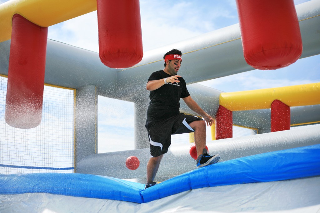 A racer runs across an inflatable ledge while dodging balls, getting hosed down and avoiding the hanging columns in the Slippery Slopes obstacle.