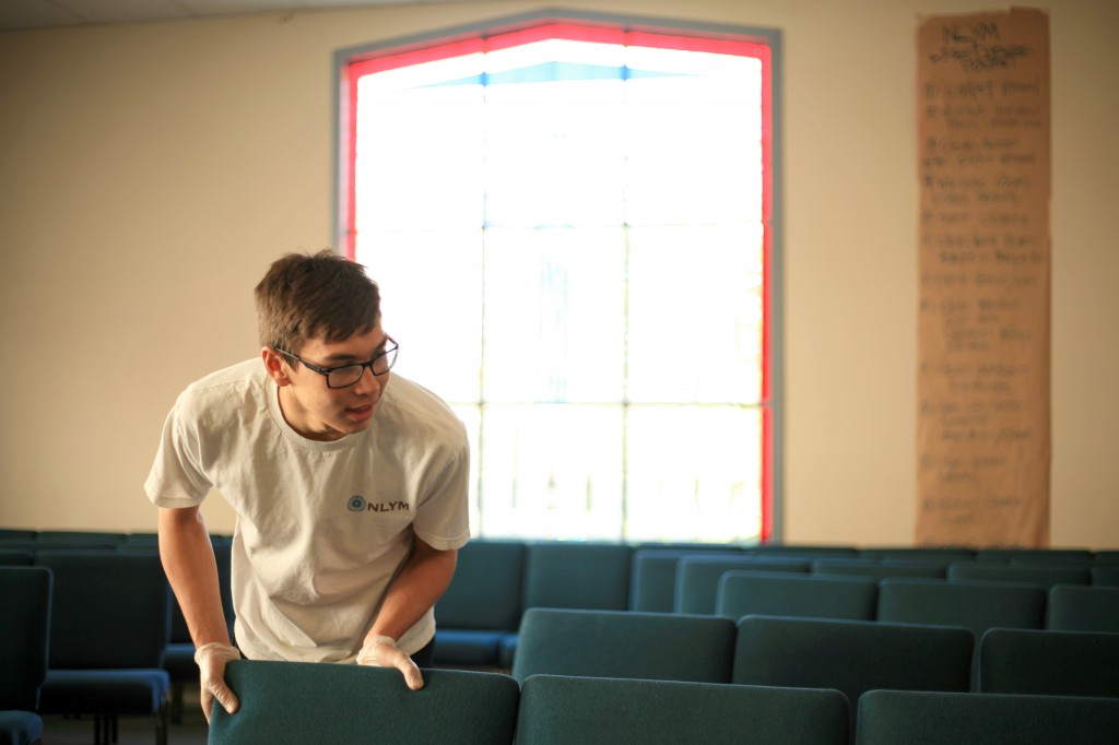 Jake Whelan, 15, a sophomore at Newport Harbor High School, arranges chairs in the congregational hall after the young men removed the carpet and cleaned the room. New carpet will be installed by professionals soon.