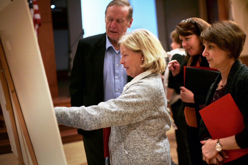 Doris Townsend (center) points to an area on a map of Newport Beach that highlights the liquefaction zones, as Tom Townsend (left) and Linda Marczak (far right) and others look on.