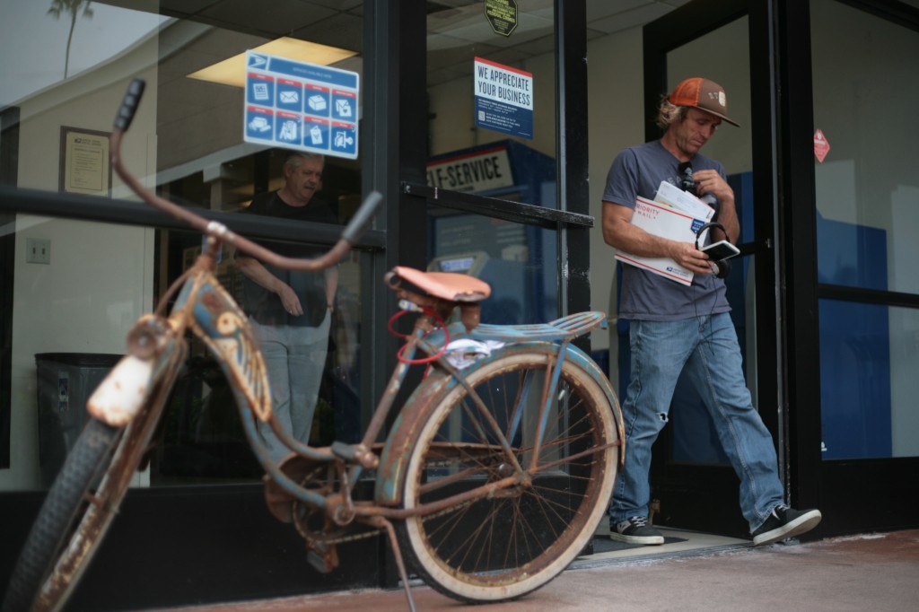 Drew Colome leaves the Bay Station Post Office on Riverside Avenue in Newport Beach on Thursday. The local, who rides his classic bike to the store, didn't know about the lease ending for USPS at the location. — Photo by Sara Hall