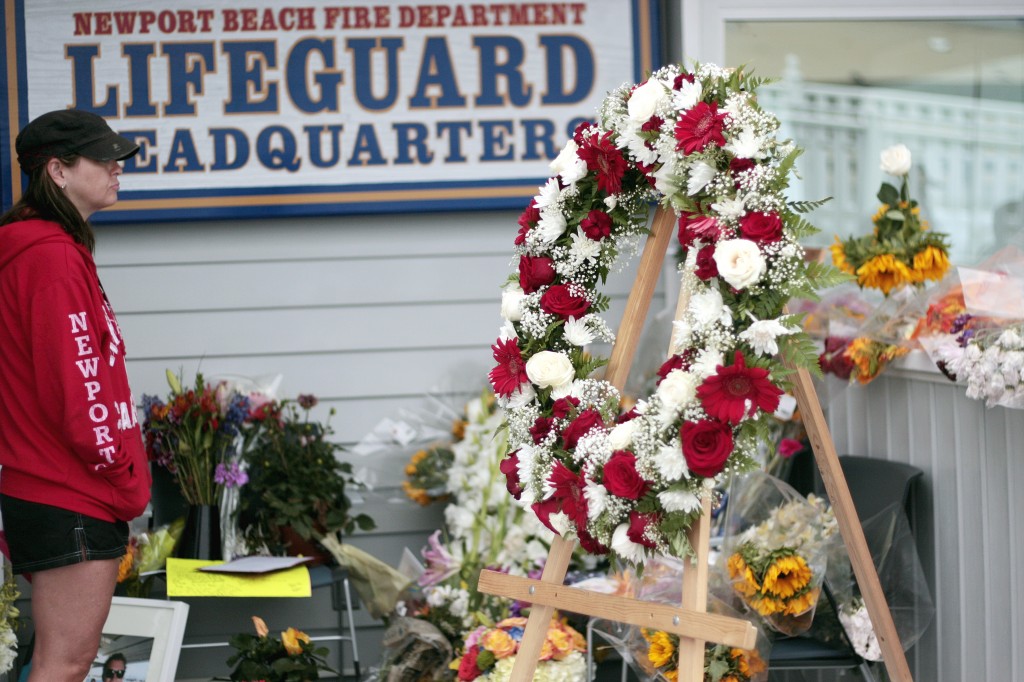 A woman pays her respects Thursday morning as she looks over the flowers, photos, cards, notes and a few flippers that have been placed at the Newport Beach Fire Department's lifeguard headquarters at the Newport Beach Pier as a memorial for Ben Carlson, the NB lifeguard veteran who died Sunday while attempting to rescue a swimmer in distress. — Photo by Sara Hall ©