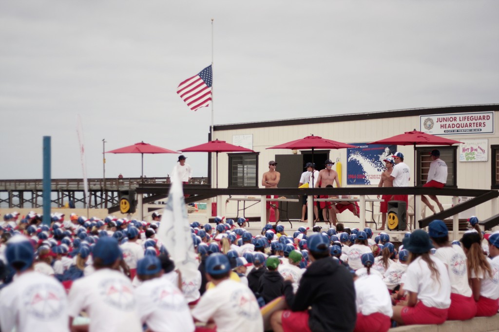 The Junior Lifeguards start their day with morning announcements on Thursday as the NBJG headquarters' flag is posted at half mast in honor of Ben Carlson. — Photo by Sara Hall ©