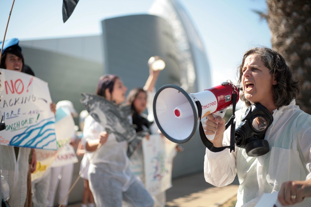  Andrea Weber, a paralegal for the Center for Biological Diversity, leads a group of protesters in a cheer Wednesday outside the Newport Beach City Hall and Civic Center while the California Coastal Commission was meeting inside council chambers. The organization, alongside various other environmental groups, was demonstrating in protest to offshore fracking. Many protesters wore gas masks and hazmat suits. The center delivered a letter urging commissioners to press the federal government for greater oversight of fracking in federal waters off California’s coast. — Photo by Sara Hall ©