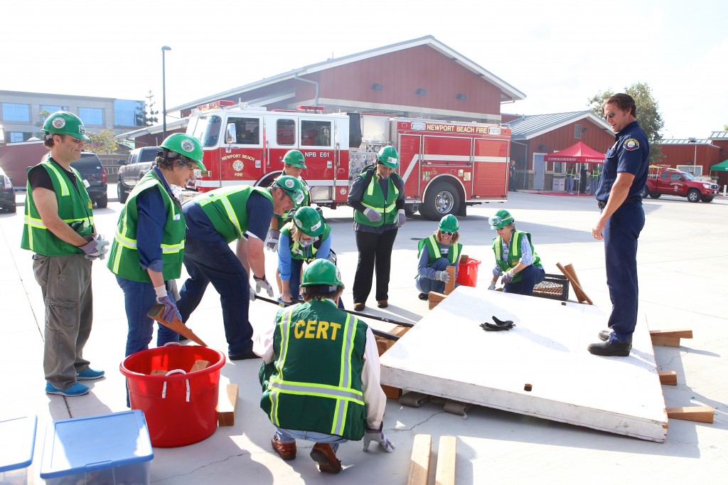 Fire engineer Alan Baker stands on a wooden wall and watches as CERT volunteers use shoring and cribbing methods to lift it off a “fire hose victim” during Drill the Skills on Saturday. Baker jumped up and down on the wall to test the stability of the box cribbing. — Photo by Jim Collins ©