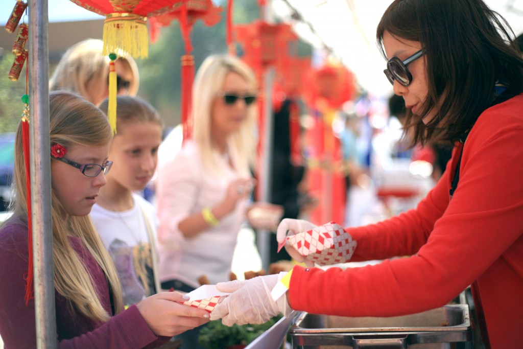 Volunteer mom Terri Wang hands Abigal Richards, 10, and Anika Ball, 11, egg rolls at the China food booth at the festival. — Photo by Sara Hall ©