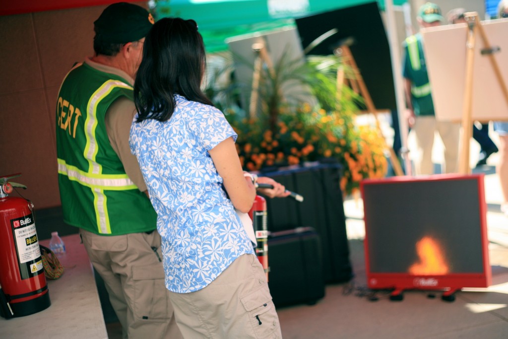 Laguna Beach CERT member Sonny Myers (left) helps Newport Beach resident Debbie Chan use an extinguisher to douse a digital fire at the expo. — Photo by Sara Hall ©