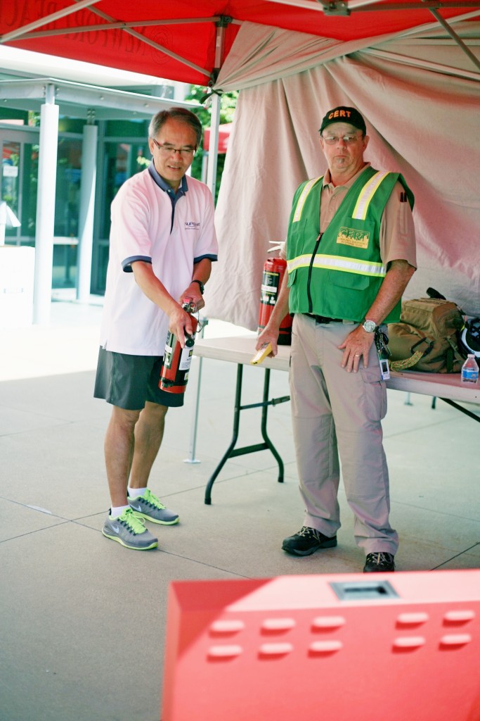 Laguna Beach CERT member Sonny Myers (right) helps Newport Beach resident Victer Chan use an extinguisher to douse a digital fire at the expo. — Photo by Sara Hall ©