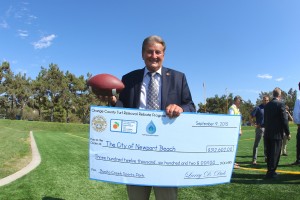 Mayor Ed Selich stands on the new synthetic turf at Bonita Creek Park, holding a rebate check from the Municipal Water District 