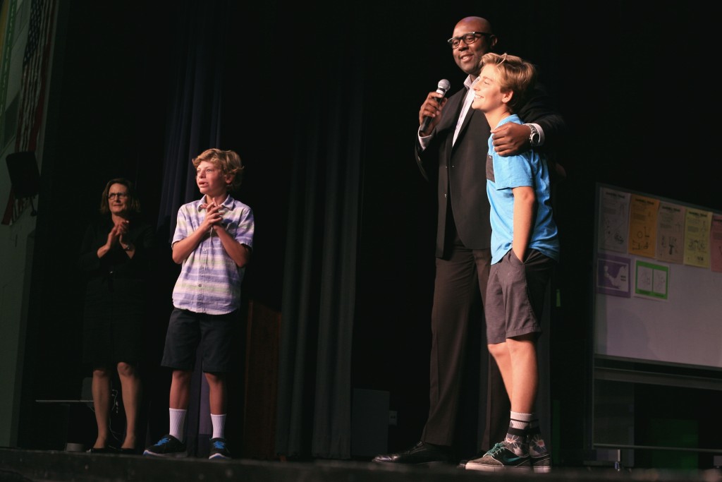 Retail expert Freddy Cameron talks to the crowd at Harbor Day School last week after surprising eighth grader Jack McKenna during an assembly showing the “Hatched” episode he was featured on. Cameron was one of the experts that reviewed McKenna’s toffee business on the TV show. McKenna’s little brother, Colin, who inspired Jack McKenna to make the toffee stands off to the side. — Photo by Sara Hall ©