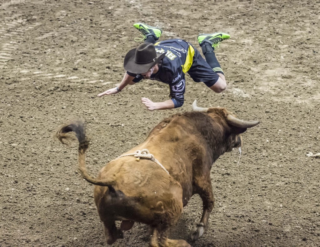 A PBR fighter flies over a bull during the event. — Photo by Lawrence Sherwin ©