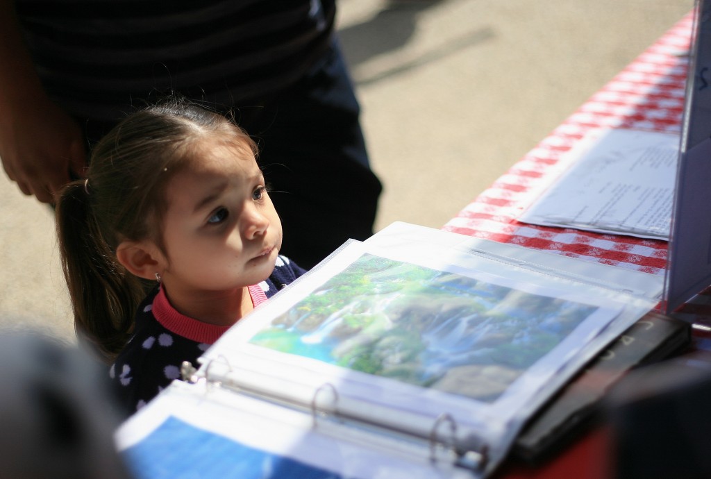 Arianna Soto, 2, watches as her “passport” booklet gets stamped. Her aunt, Melissa Iglesias, is a senior at Sage Hill. — Photo by Sara Hall ©