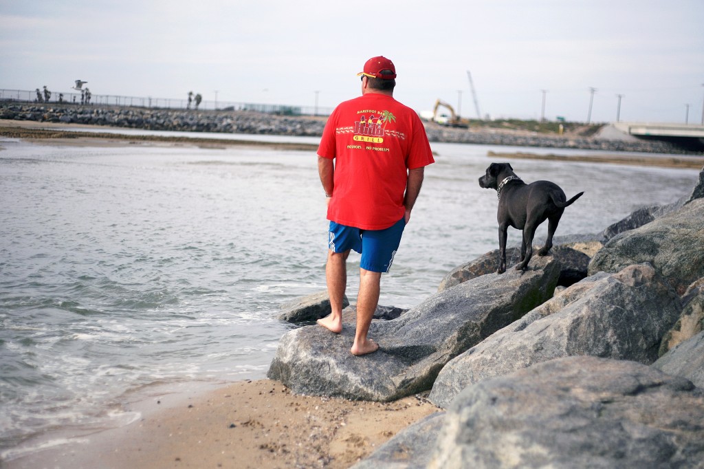 Newport Beach resident Robert Wyatt and his dog Stella, a 1-year-old rescued mixed breed pup, look out at the water from the beach near the Santa Ana River mouth on Thursday. — Photo by Sara Hall ©