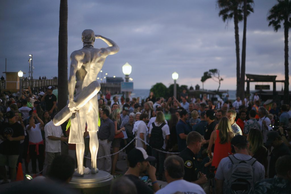 A statue depicting Ben Carlson, the first Newport Beach lifeguard to die in the line of duty, watches over the crowd and beach after an unveiling ceremony on Wednesday night. — Photo by Sara Hall ©