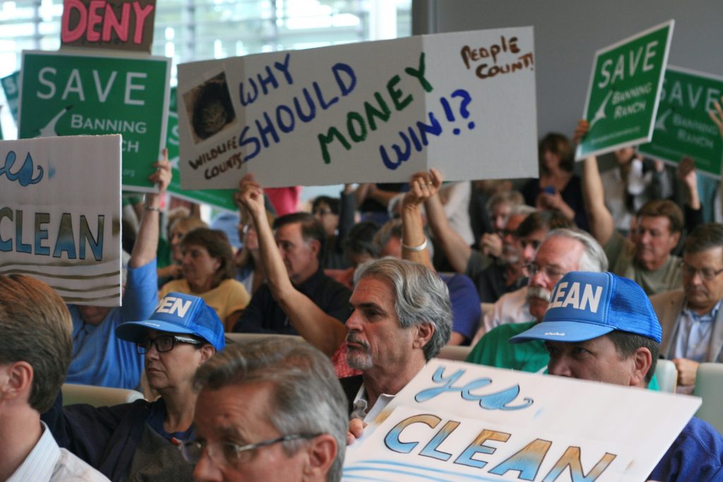 Senior Project Manager for Newport Banning Ranch Mike Mahler (center) said sits in between Banning Ranch project protesters and supporters as they wave signs during the California Coastal Commission meeting on Sept. 7. — Photo by Sara Hall ©