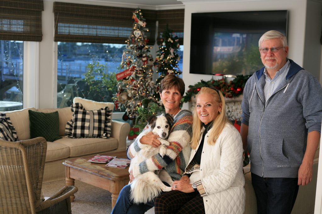 (left to right) 20th Annual Balboa Island Holiday Home Walking Tour homeowner participant Diana Conners (holding her dog, Dewey), tour docent and Balboa Island Improvement Association board member Kristine Taft, and tour chair and BIIA board member Tom Popplewell, pose for a photo in Conner’s living room. — Photo by Sara Hall ©