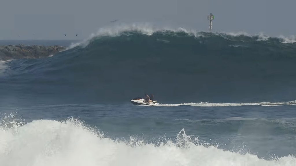 A couple tries to outrun a large wave on a personal watercraft jet ski, before getting tossed into the ocean near the Wedge. — Photo courtesy SoCalVideos ©