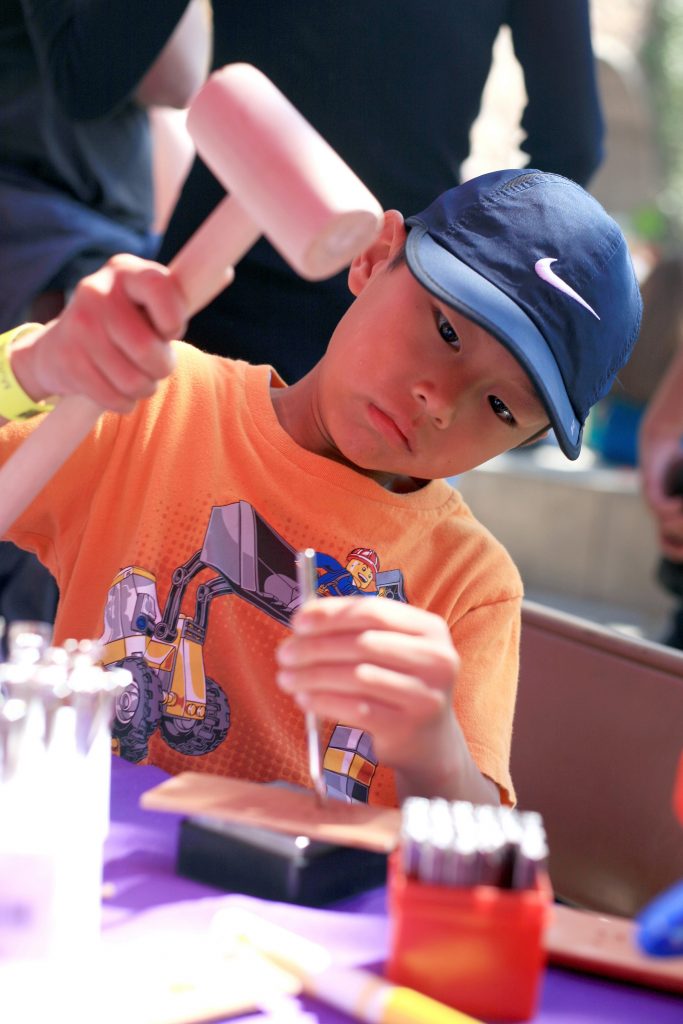 Peyton Lau, 7, of Irvine hammers in a stamp into a leather bracelet at a craft booth at the fair. — Photo by Sara Hall ©