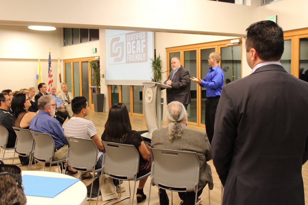 Deaf United CEO Lamar Stewart speaks to the crowd at the event as an interpreter translates into sign language as Mayor Kevin Muldoon stands on the side (foreground) and watches. — Photo by Victoria Kertz ©