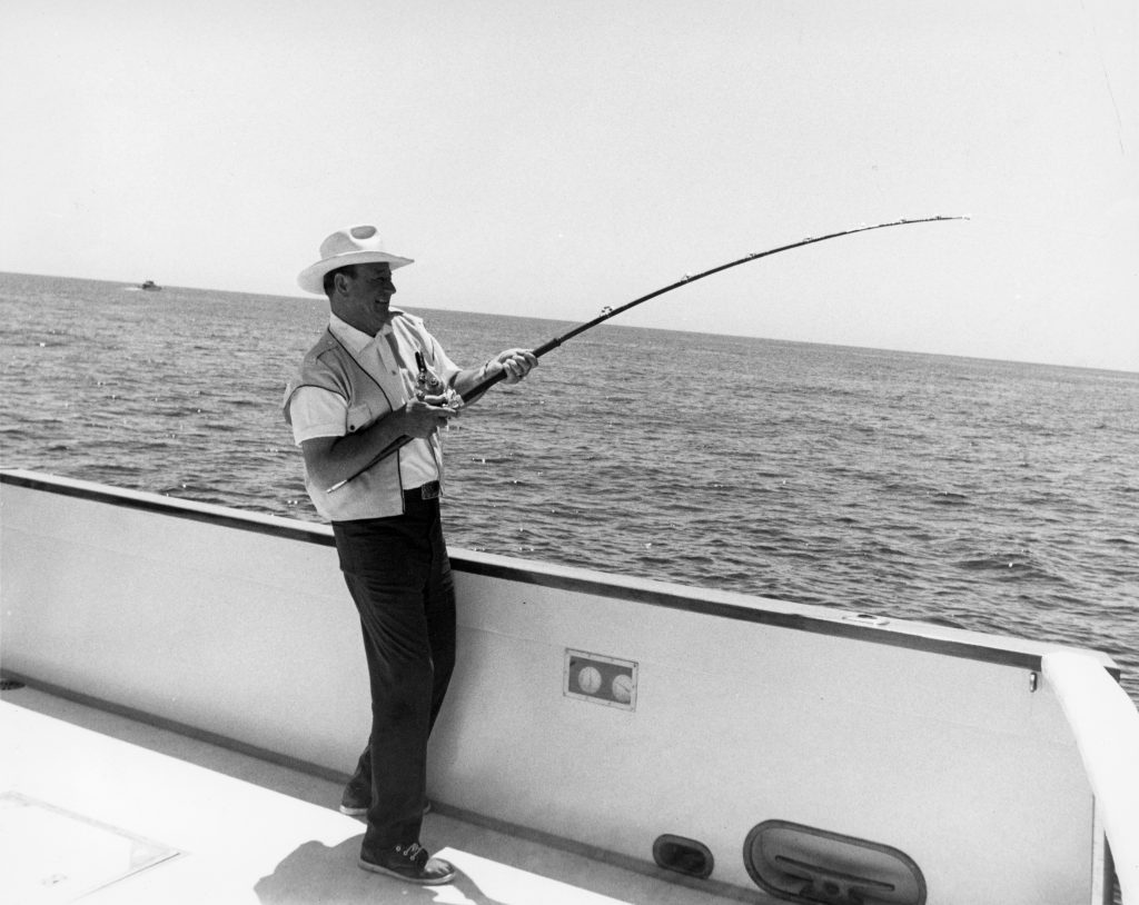 John Wayne fishing off the side of his boat, the Wild Goose. He loved to sail and often visited Catalina Island. — Photo courtesy John Wayne Enterprises ©