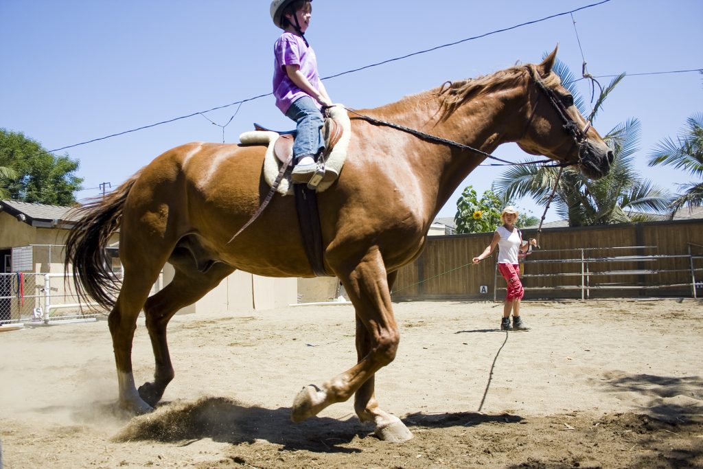 Bernadette Olsen holds a lead and helps Connor McCrury, 8, trot Scruffy around the dusty backyard arena at Back Bay Therapeutic Riding Club. Connor’s mother said his confidence has increased dramatically since he began the program in May. — Photo by Sara Hall ©