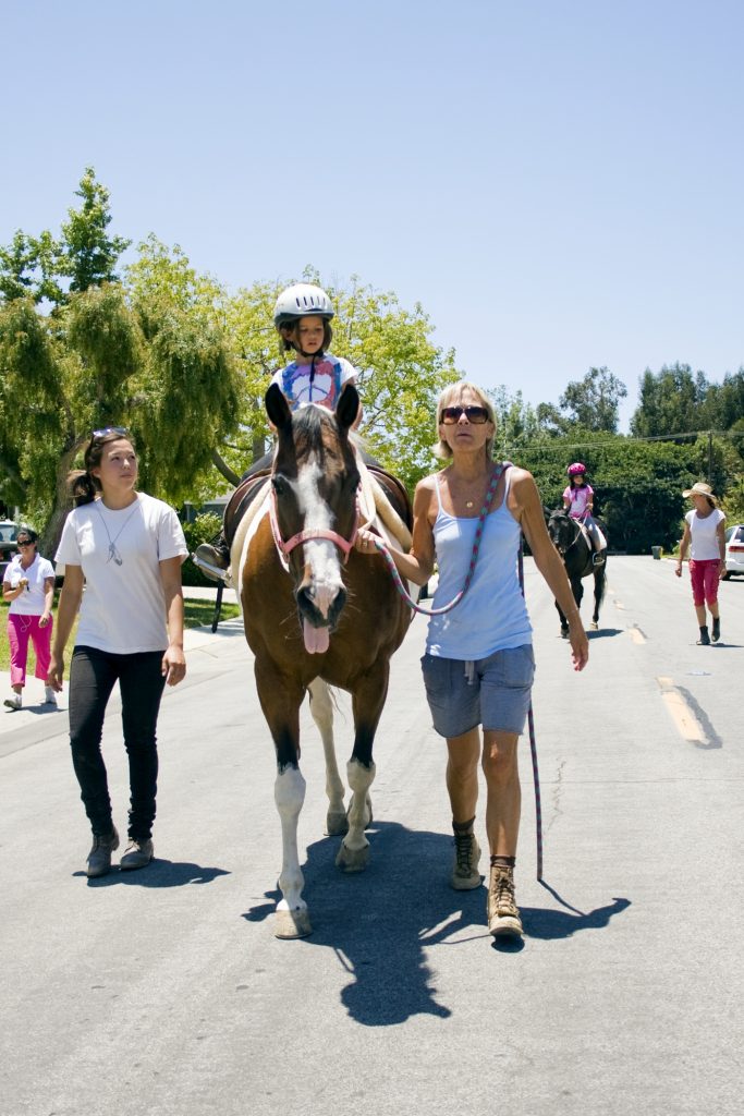 Back Bay Therapeutic Riding Club (BBTRC) student sisters Katie, 7, (front) and Karoline Shannon, 9, ride horses during their weekly session. The group that walks with them in support, from left to right, is their mother, Katherine, volunteer Katharina Chiu, horse manager Vickie Tombrello, and BBTRC founder Bernadette Olsen. — Photo by Sara Hall ©