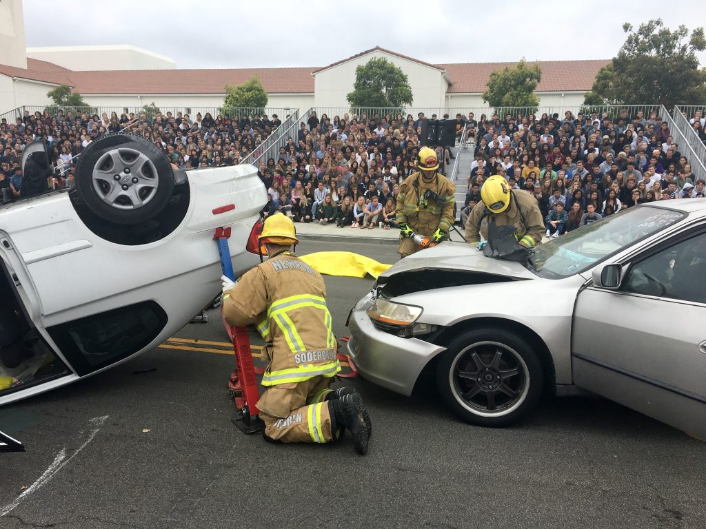 Newport Beach firefighters work to extract student participants in the "Every 15 Minutes" simulated collision on Wednesday as the rest of the Newport Harbor High School watches the scene unfold. — Photo courtesy of Newport Beach Fire Department ©