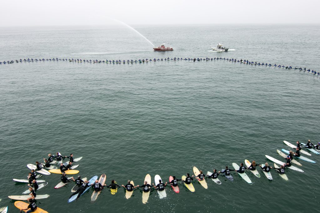 Surfers hold hands to form a circle as they break a world record and the Orange County Sheriff's Harbor Patrol boat sprays water into the air in the background. — Photo by Jim Collins ©