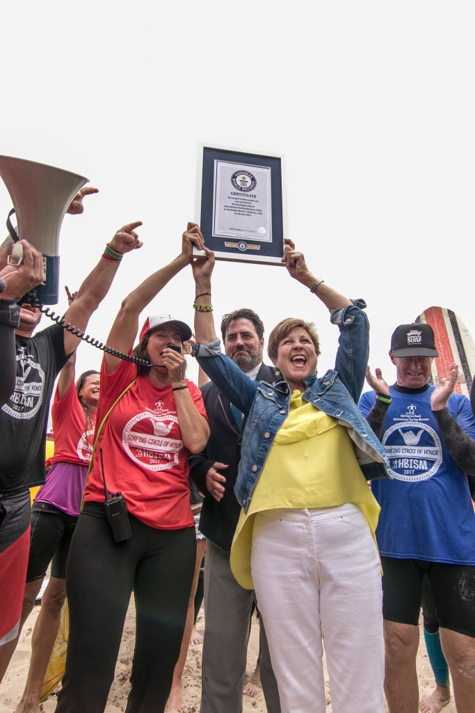 Huntington Beach Mayor Barbara Delgleize (center) holds the Guinness World Record certificate for largest surfing paddle out and cheers alongside HB International Surfing Museum Executive Director Diana Dehm (left), the Guinness World Records official (middle, background), and others. — Photo by Jim Collins ©